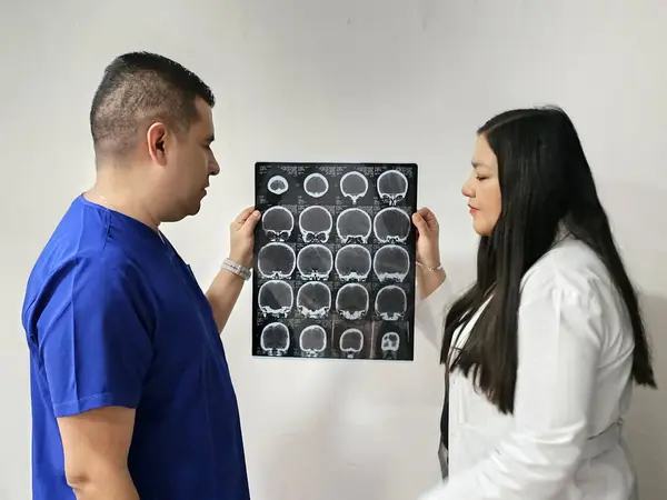Latina neurologist specialist doctor woman and dark-skinned male nurse review patient\'s brain x-ray to discuss extraordinary case study and research