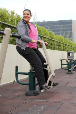 40 yaşındaki Latin kadın, dairesinin çatı bahçesinde yüksek tansiyon ve şeker hastalığını önlemek için kamu ekipmanları üzerinde egzersiz yapıyor.