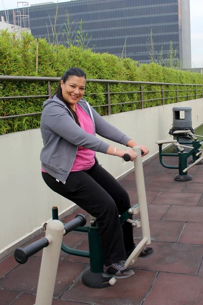 40-year-old Latina woman exercises on public equipment in the roof garden of her condominium to lose weight and prevent hypertension and diabetes