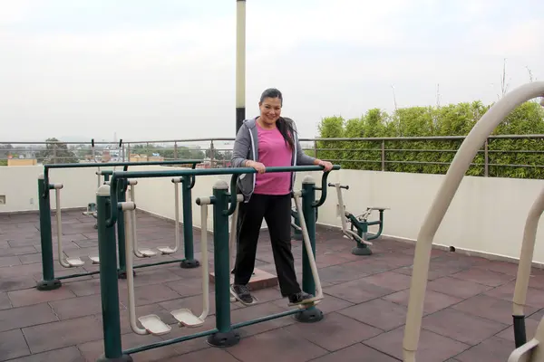 40-year-old Latina woman exercises on public equipment in the roof garden of her condominium to lose weight and prevent hypertension and diabetes