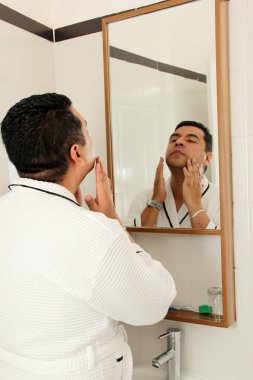 40 yaşında esmer tenli bir Latin sabah ve gece cilt bakımı yapıyor. Nokta ve kırışıklıklardan kaçınmak için serum, krem ve koruyucu kullanıyor.