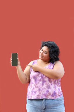20 yaşında, aşırı kilolu Latin bir kadın cep telefonunun ekranını gösteriyor. Terfi ve indirimlerden çok memnun.