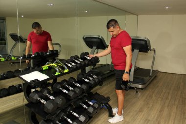 Koyu tenli Latin yetişkin adam kaza ve tıbbi ameliyat için dambılla kol rehabilitasyonu yapıyor.