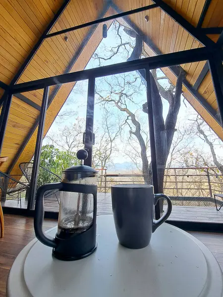 Preparing coffee in a French press or plunger coffee maker inside a cabin in the middle of the forest as a symbol of relaxation and luxury