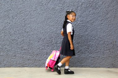 Gözlüklü, üniformalı ve sırt çantalı 4 yaşındaki Latin esmer kız okula geri dönüyor.