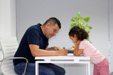 3 yaşındaki bir kız, ofisinde bir psikologla terapi görüyor, otizm ve hiperaktivite tedavisi için oyun terapisi olarak oynuyor ve çiziyor.