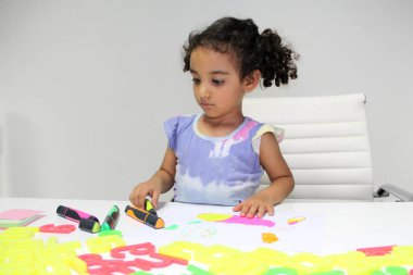 3 yaşındaki kıvırcık saçlı Latin esmer kız otizm ve dikkat eksikliği hiperaktivite bozukluğu tedavisi için çizim yapıyor.
