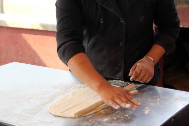 Pizzacının elleri hamuru yoğurur, yuvarlak iğne ve unla pizza tabanı için şekiller hazırlar.