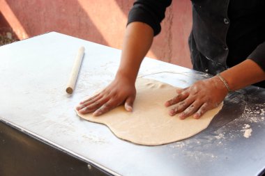 Pizzacının elleri hamuru yoğurur, yuvarlak iğne ve unla pizza tabanı için şekiller hazırlar.