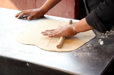 Pizzacının elleri hamuru yoğurur, yuvarlak iğne ve unla pizza tabanı için şekiller hazırlar.