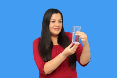 Latin yetişkin bir kadın sıcak hava dalgasında su içmek için içtiği cam bardağı gösteriyor.