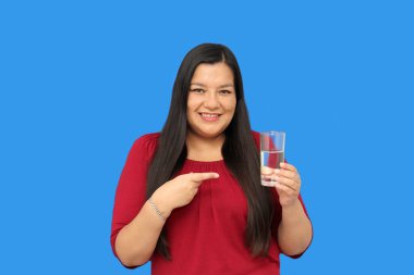 Latin yetişkin bir kadın sıcak hava dalgasında su içmek için içtiği cam bardağı gösteriyor.