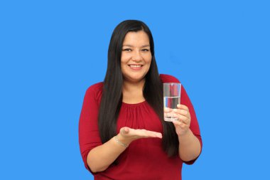 Latin yetişkin bir kadın sıcak hava dalgasında su içmek için içtiği cam bardağı gösteriyor.