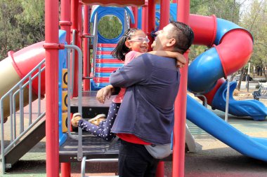 Divorced single dad plays with his brunette latina daughter in playground park spins and hugs spend fun time