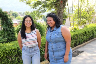 İki genç kız kardeş ve esmer Latin arkadaşlar okuldan sonra parkta yürüyüp sohbet ediyorlar.