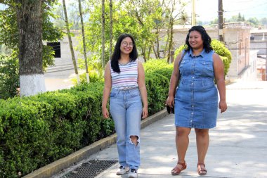 İki genç kız kardeş ve esmer Latin arkadaşlar okuldan sonra parkta yürüyüp sohbet ediyorlar.