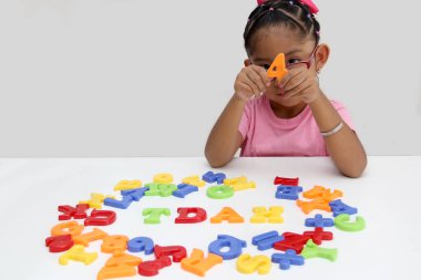 4 yaşındaki Latin esmer kız renkli harflerle oynuyor ve İspanyolca 'da dikkat eksikliği hiperaktivite bozukluğu anlamına gelen TDAH kelimesini oluşturuyor.