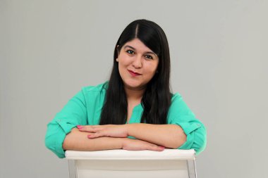 30 yaşındaki Latin kadın bir ofis koltuğunda oturuyor ve mesleki gelişiminden memnun ve mutlu görünüyor.