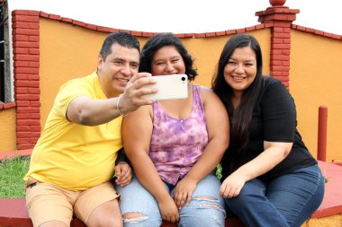 Baba, anne ve genç esmer tenli Latin kızı cep telefonlarını kullanarak video çekiyor, alışveriş yapıyor, selfie çekiyor ve birlikte iyi vakit geçiriyorlar.