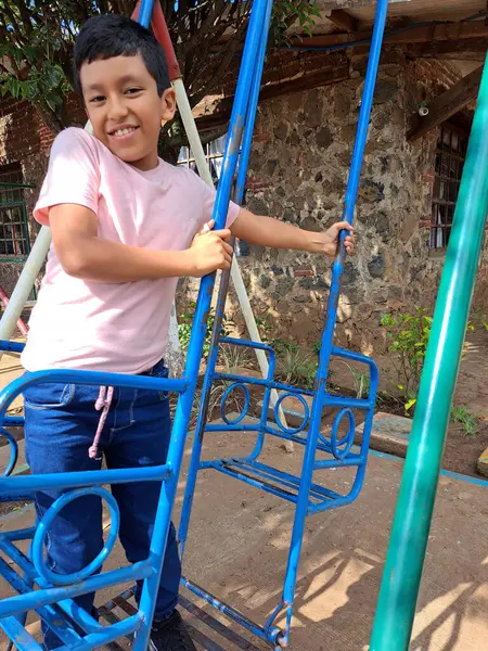 stock image 8-year-old dark-skinned Latino boy plays on the playground, swings on the swing, has fun in the park as therapy for attention deficit hyperactivity disorder ADHD