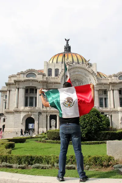 stock image Mexico City, Mexico - Sep 6 2023: Man holds the Mexican flag in front of the Palacio de Bellas Artes to celebrate the national holidays of independence and revolution