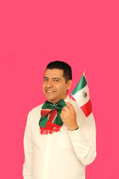 stock image Dark-skinned Mexican adult man with tricolor bow proudly shows the flag of Mexico to celebrate the national holidays