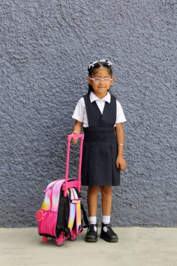 4 yaşındaki Latin esmer kız okula bu üniformayı giymiş olarak sırt çantasıyla gidiyor.