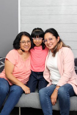 Üç kuşak esmer Latin kadın: gözlüklü büyükanne, anne ve kız sevgilerini gösterip Anneler Günü 'nü kutluyorlar.