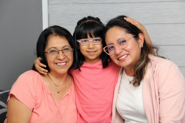 Üç kuşak esmer Latin kadın: gözlüklü büyükanne, anne ve kız sevgilerini gösterip Anneler Günü 'nü kutluyorlar.