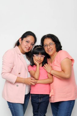 Three generations of brunette Latina women with glasses, grandmother, mom and daughter hug each other and show their love to celebrate Mother's Day clipart