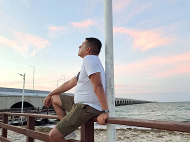 Esmer tenli Latin yetişkin adam Progreso Yucatan Meksika denizinde gün batımını izliyor.