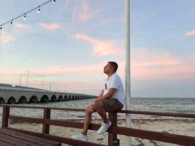 Esmer tenli Latin yetişkin adam Progreso Yucatan Meksika denizinde gün batımını izliyor.