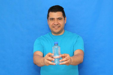 Koyu tenli Latin bir adam 40 yaşında, su dolu plastik bir şişe gösteriyor çünkü sağlıklı bir hayat için su önemli.