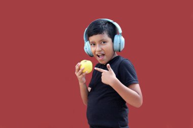 9 yaşındaki koyu tenli, kulaklıklı Latin çocuk müzik dinlerken elma yiyor.
