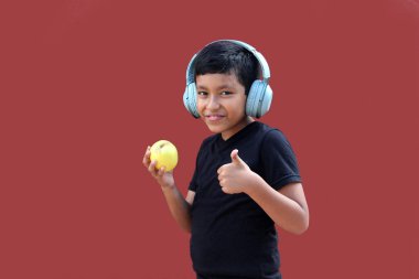 9 yaşındaki koyu tenli, kulaklıklı Latin çocuk müzik dinlerken elma yiyor.