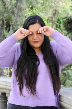 40 yaşındaki uzun düz saçlı Latin kadın gözlerini ovuşturuyor çünkü çevredeki alerji ve kirlilik yüzünden yanıyor ve acıyor.