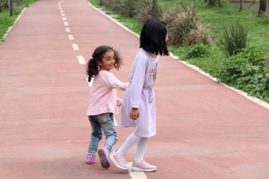 Brunette Latina 4 and 5 year old girls walk holding hands like sisters and friends spending time together outdoors clipart