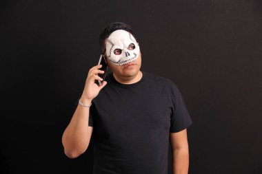 Kafatası maskeli Meksikalı yetişkin adam cep telefonunu Ölüler Günü terfilerinden ve Meksika 'daki indirimlerden yararlanmak için kullanıyor.
