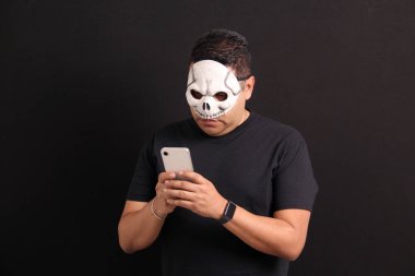 Kafatası maskeli Meksikalı yetişkin adam cep telefonunu Ölüler Günü terfilerinden ve Meksika 'daki indirimlerden yararlanmak için kullanıyor.
