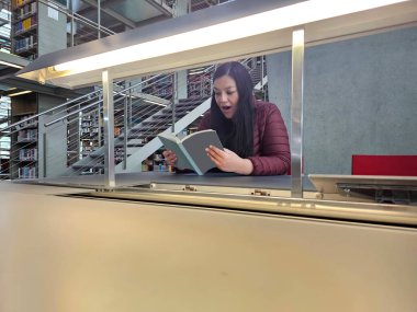 40 yaşında bekar bir Latin kadın kütüphanede ders çalışmak ve bilgi edinmek ve sessiz vakit geçirmek için kitap okuyor.