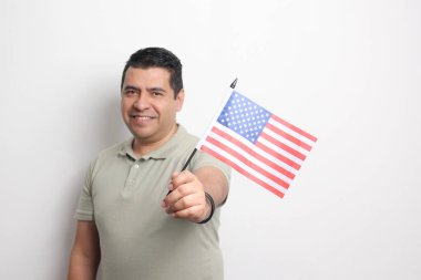 40 yaşında esmer tenli Latin bir adam Amerika topraklarında göçmen olarak yaşayan Amerika Birleşik Devletleri bayrağını gösteriyor.