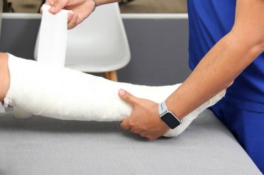 Erkek latin doktor, bacağında kırık olan esmer kadın hastayla ilgilenir.