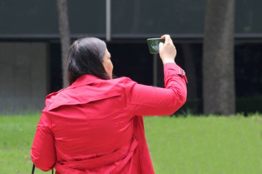 40 yaşında Latin bir kadın cep telefonuyla parkta yürüyor. Uzaktan çalışmak için, dışarıda video görüşmeleri yapıyor.