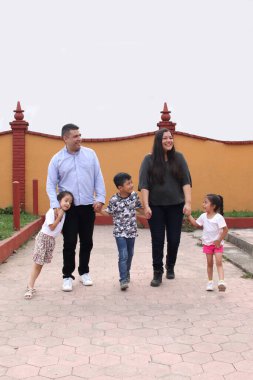 Baba, anne, kız ve oğlanın esmer Latin ailesi parkta el ele yürür.
