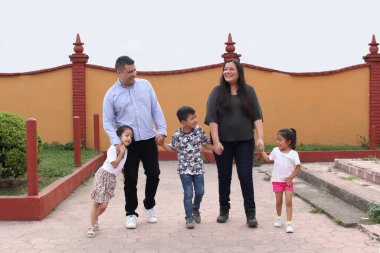 Baba, anne, kız ve oğlanın esmer Latin ailesi parkta el ele yürür.