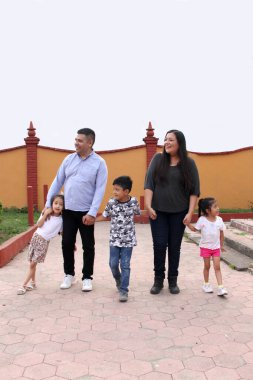 Baba, anne, kız ve oğlanın esmer Latin ailesi parkta el ele yürür.