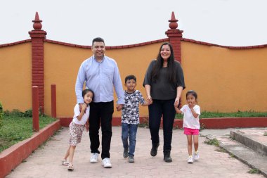 Baba, anne, kız ve oğlanın esmer Latin ailesi parkta el ele yürür.