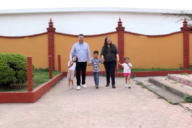 Baba, anne, kız ve oğlanın esmer Latin ailesi parkta el ele yürür.