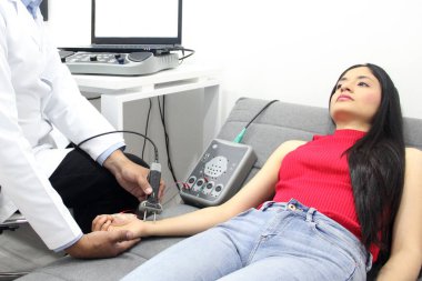 Koyu tenli Latin nörolog doktor kadın hastanın kolunda elektromiyografi ve somaduyusal canlandırma potansiyelleri üzerinde çalışıyor.