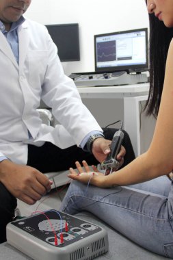 Koyu tenli Latin nörolog doktor kadın hastanın kolunda elektromiyografi ve somaduyusal canlandırma potansiyelleri üzerinde çalışıyor.
